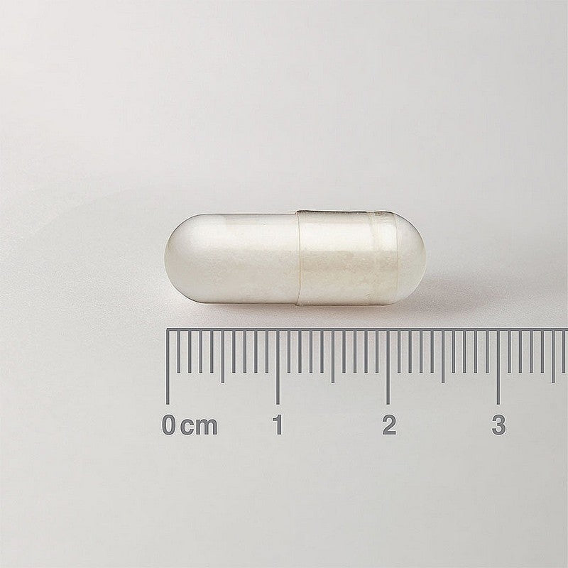 White capsule pill on a light gray background with a ruler for scale.